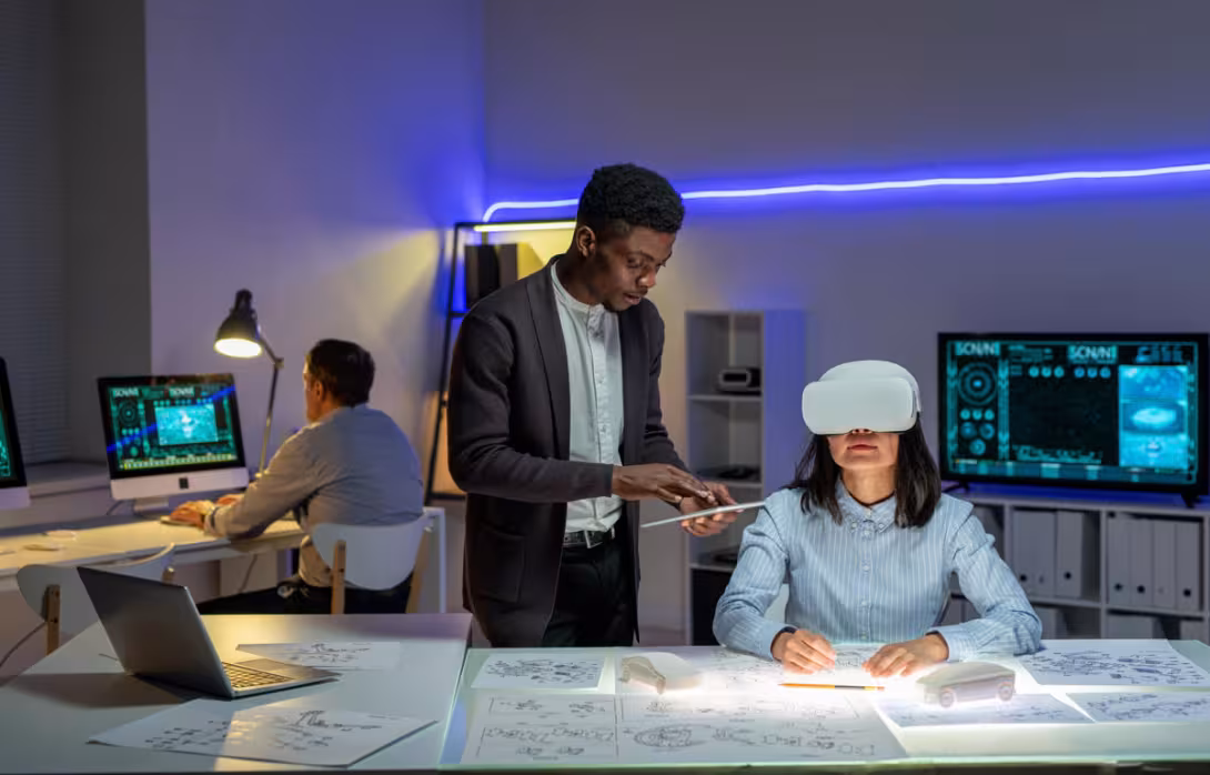 A designer explores a 3D car model using a VR headset, blending immersive technology with hands-on engineering. Nearby, teammates collaborate through tablets and multi-monitor setups, driving innovation in a dynamic, tech-powered workspace.